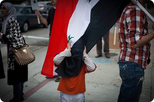 A boy hides behind the Syrian flag held by an actvist at a rally in support of Arab anti-goverment revolutions on Saturday afternoon outside the Federal Building on Wilshire Blvd.